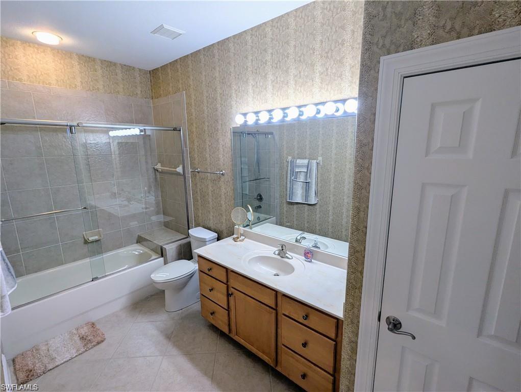 Bathroom with wallpapered walls, vanity, light tile patterned floors, and combined bath / shower with glass door