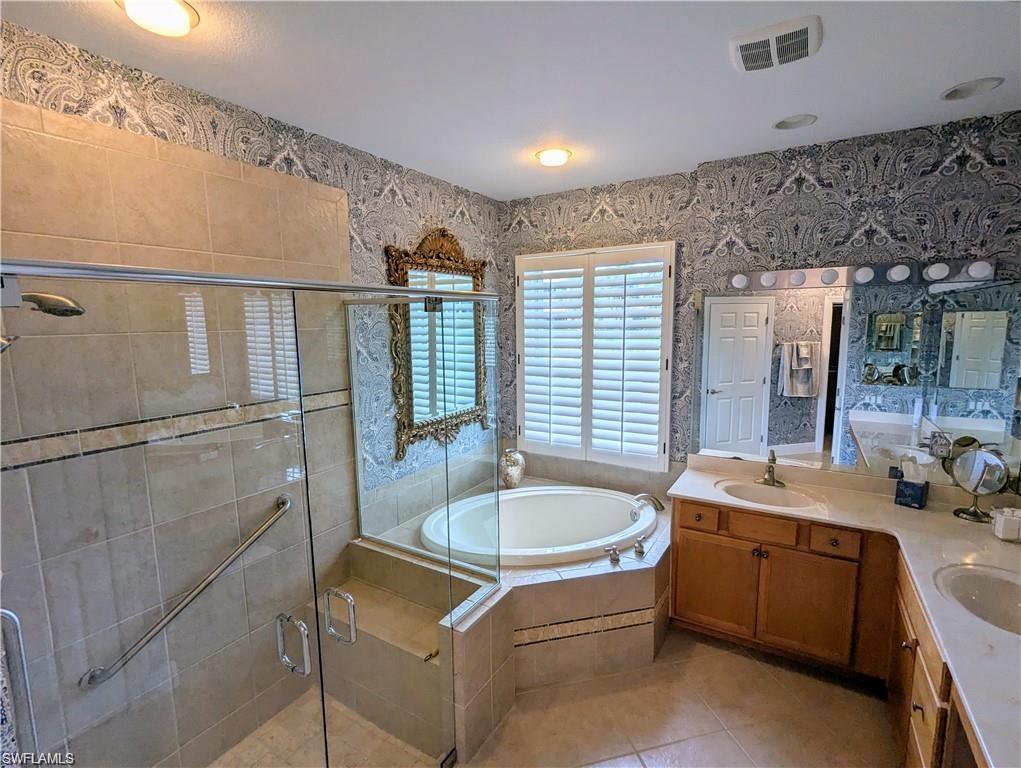Full bath featuring double vanity, wallpapered walls, a bath, a stall shower, and light tile patterned flooring