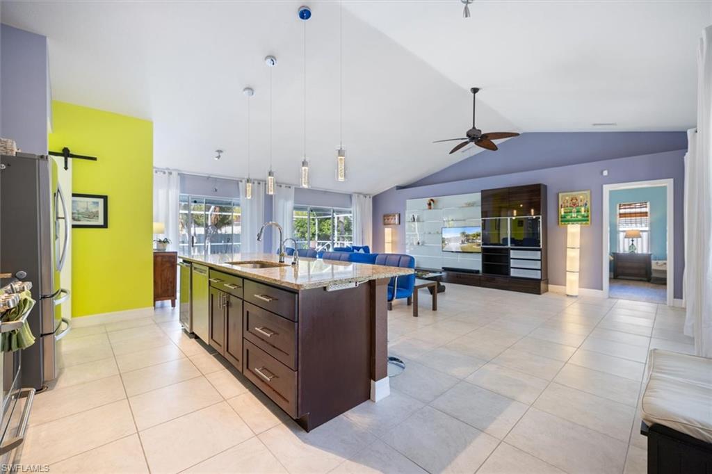 Kitchen featuring lofted ceiling, pendant lighting, dark brown cabinets, a center island with sink, and open floor plan