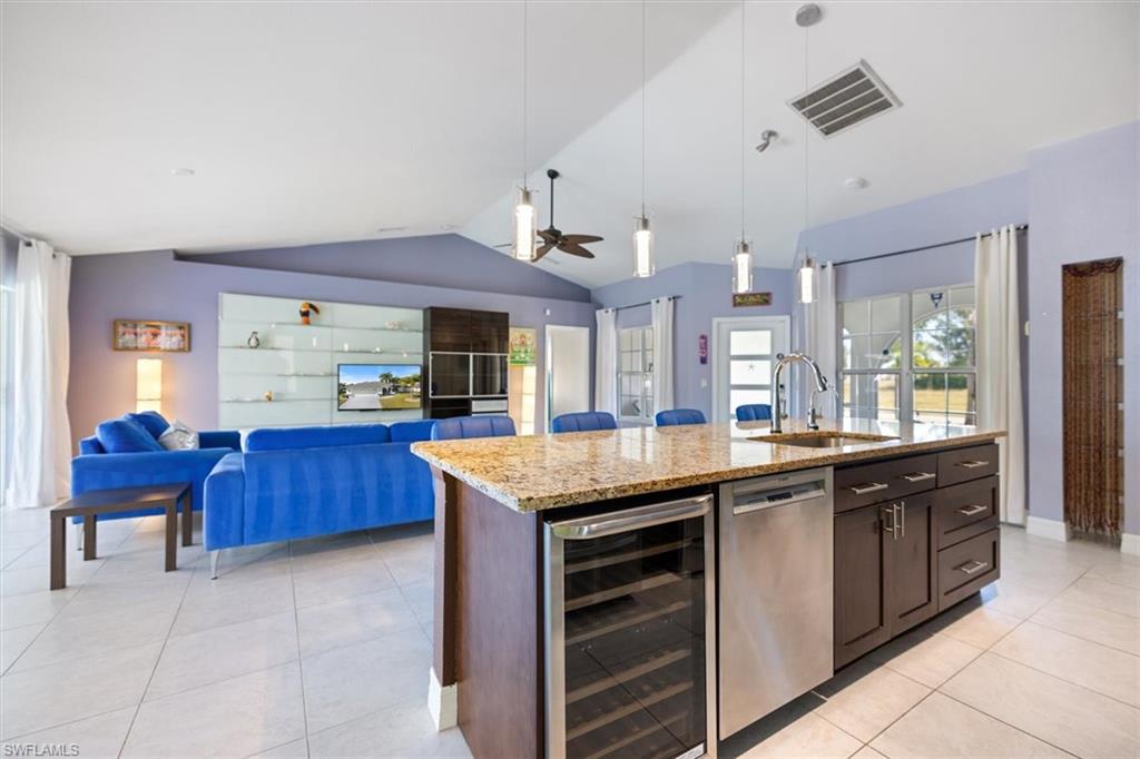 Kitchen with open floor plan, wine cooler, light stone countertops, hanging light fixtures, and dark brown cabinets