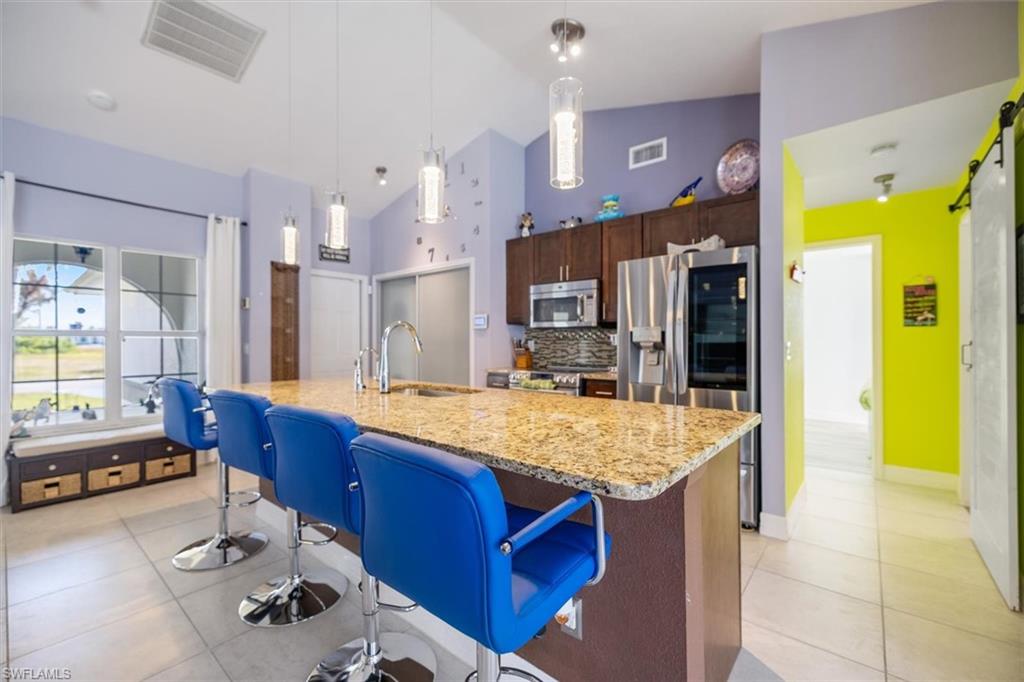 Kitchen featuring backsplash, dark brown cabinetry, appliances with stainless steel finishes, a breakfast bar area, and decorative light fixtures