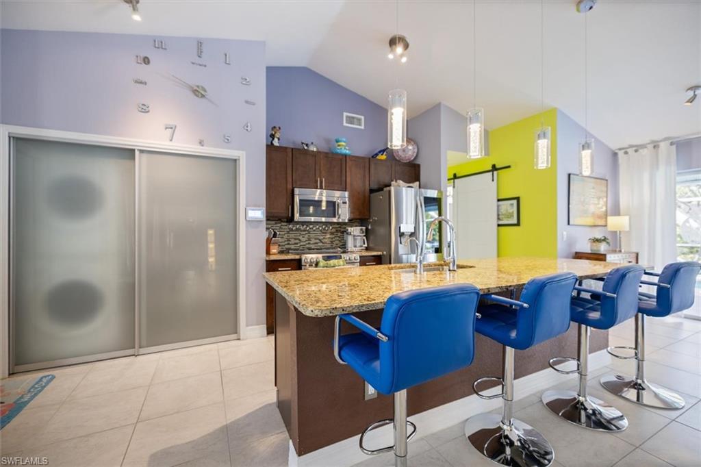 Kitchen with dark brown cabinets, a kitchen bar, tasteful backsplash, appliances with stainless steel finishes, and light stone countertops
