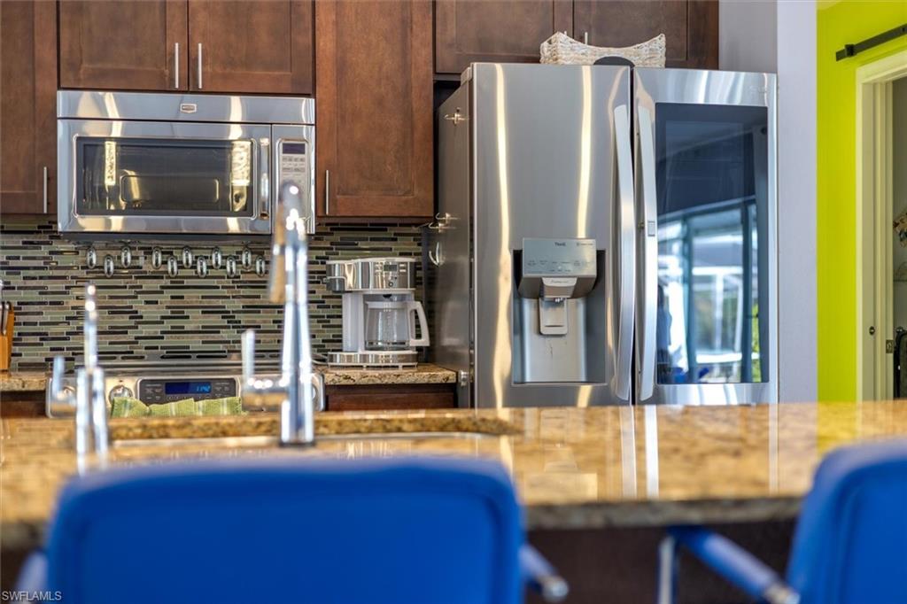 Kitchen featuring stainless steel appliances, tasteful backsplash, light stone countertops, and dark brown cabinets