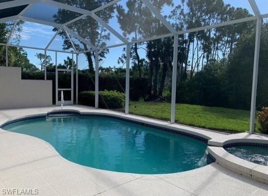 View of swimming pool with an in ground hot tub, a yard, glass enclosure, and a patio area