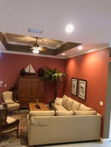 Living room featuring a raised ceiling, ceiling fan, and crown molding