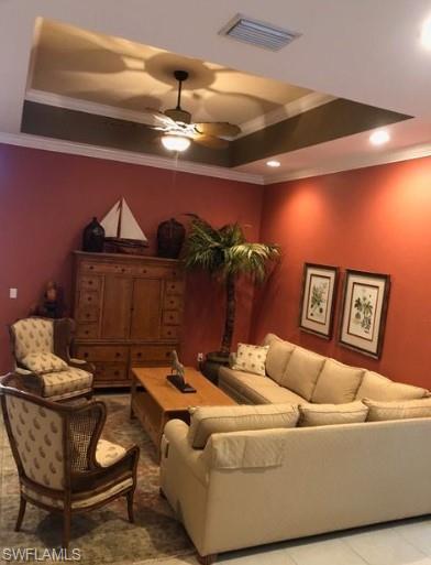 Tiled living room featuring ceiling fan, a raised ceiling, and ornamental molding