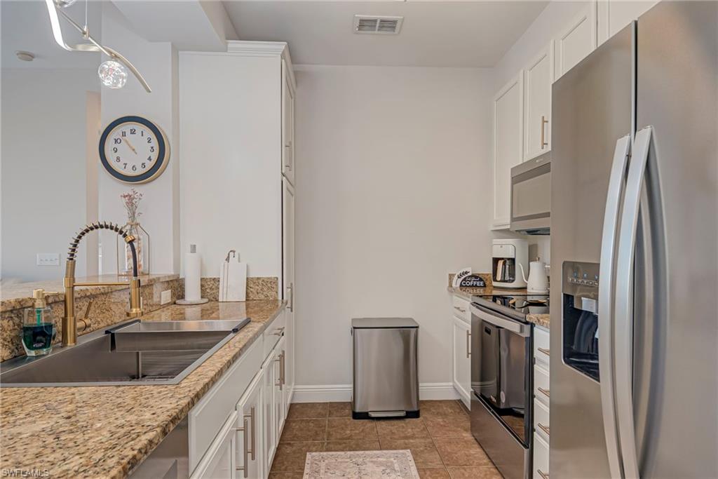Kitchen featuring stainless steel appliances, white cabinets, light stone counters, pendant lighting, and a chandelier