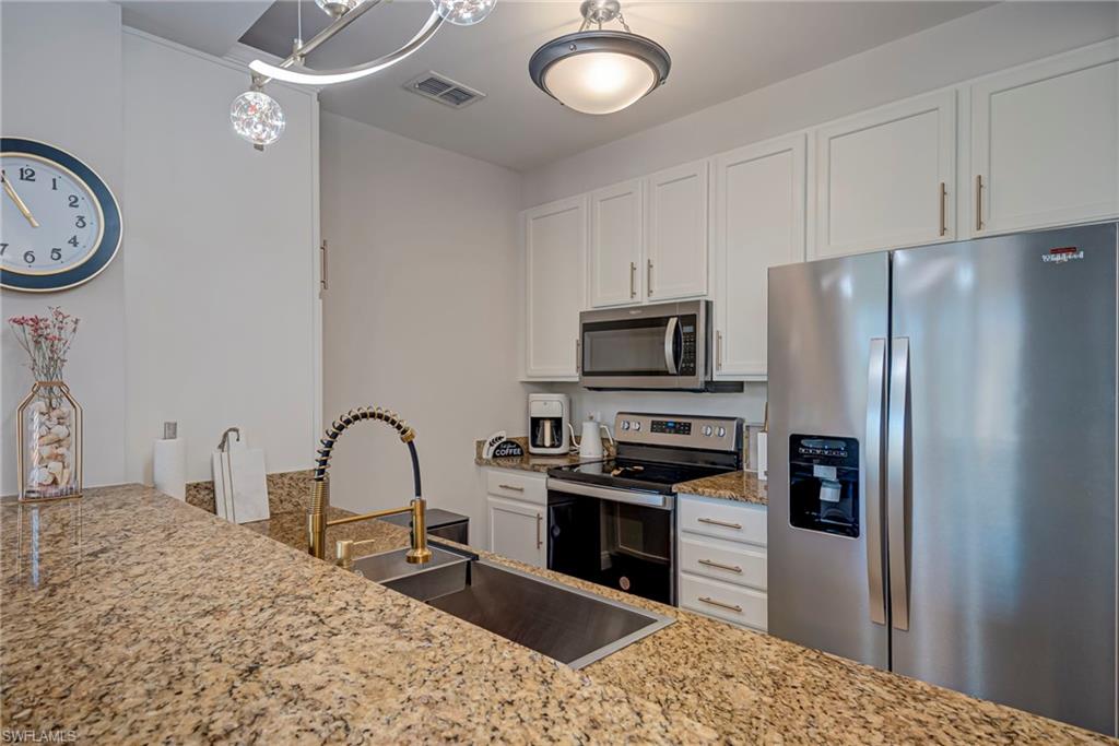 Kitchen featuring light stone countertops, white cabinetry, light flooring, stainless steel appliances, and pendant lighting