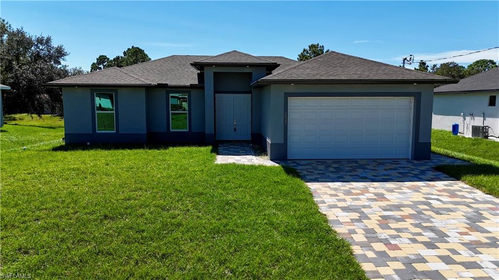 View of front of house with a front yard, decorative driveway, stucco siding, and roof with shingles