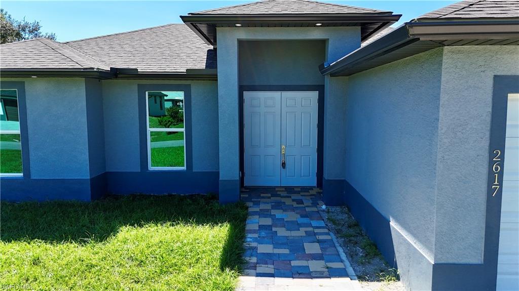 Property entrance featuring stucco siding and a shingled roof