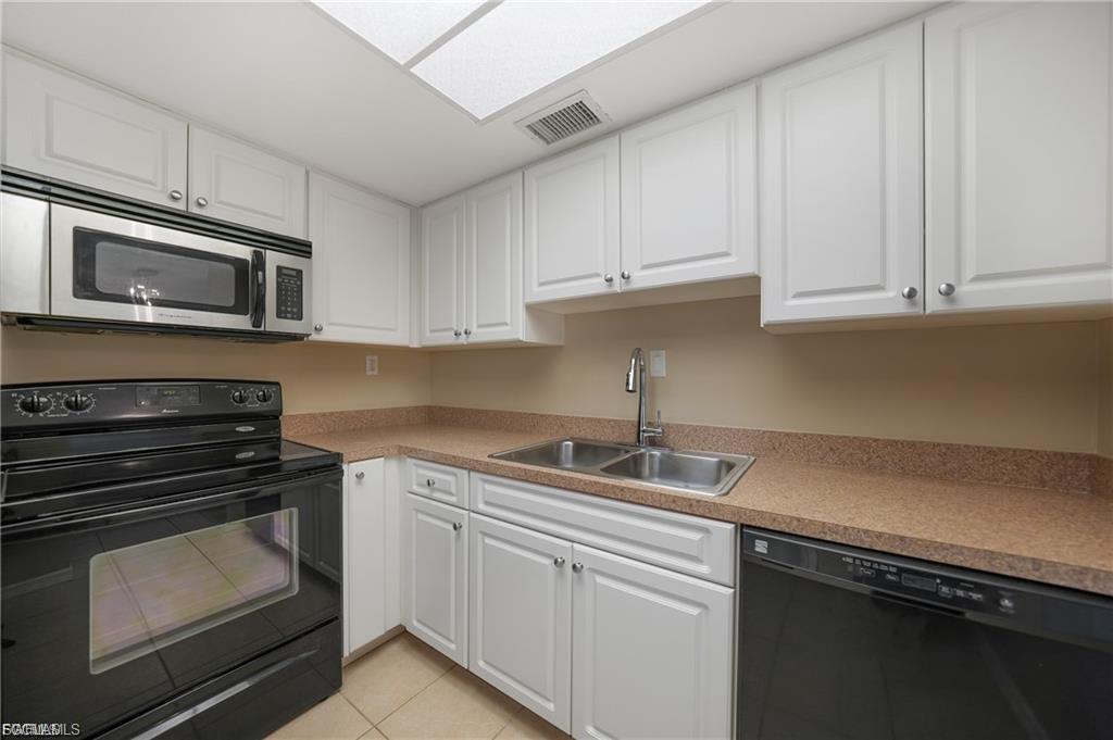 Kitchen featuring black appliances, white cabinetry, light tile patterned floors, and light countertops