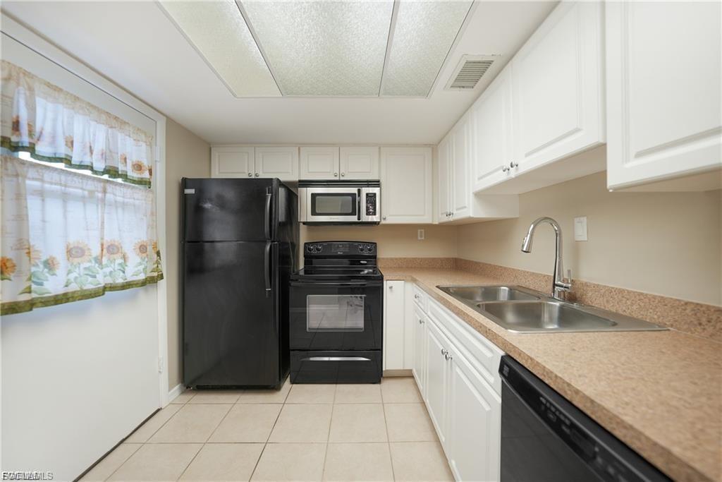 Kitchen featuring black appliances, light countertops, light tile patterned flooring, and white cabinets