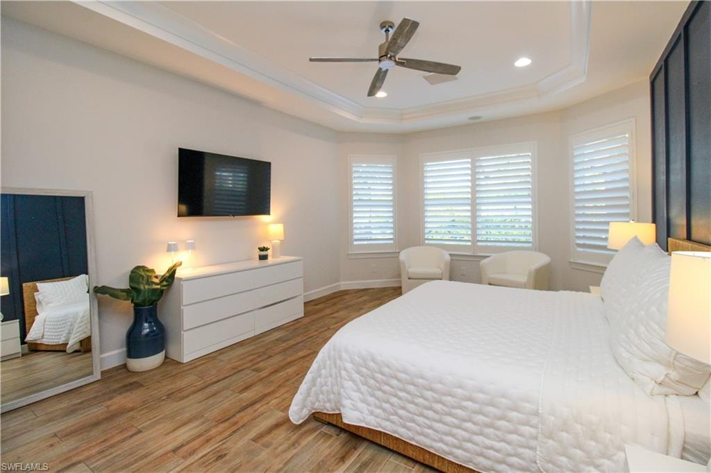 Bedroom with hardwood / wood-style flooring, a raised ceiling, and ceiling fan