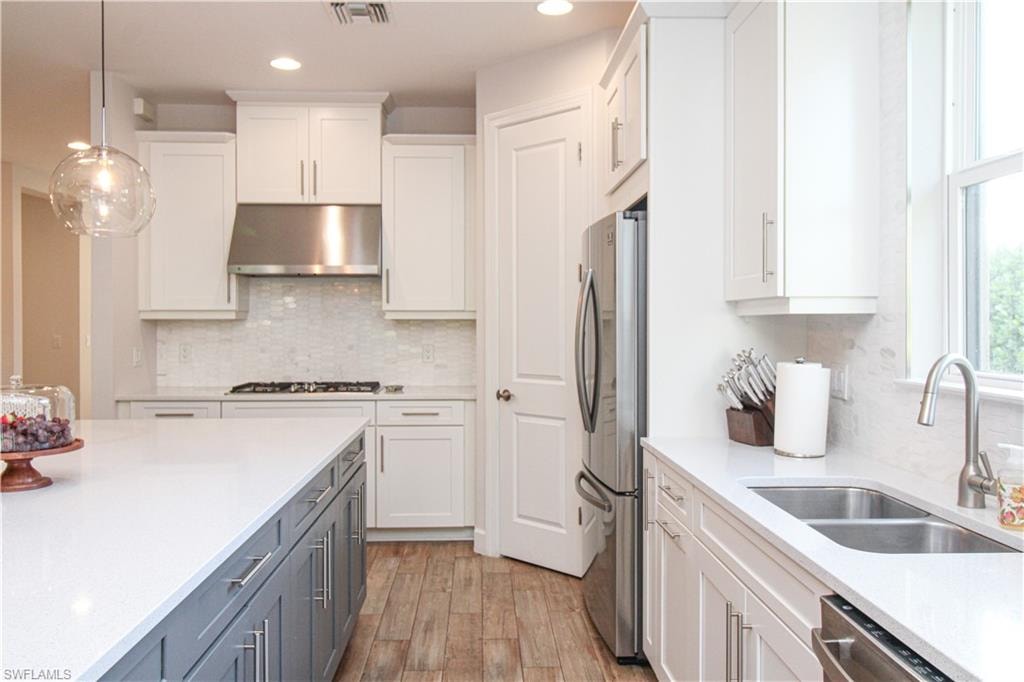 Kitchen featuring sink, ventilation hood, decorative light fixtures, white cabinets, and appliances with stainless steel finishes