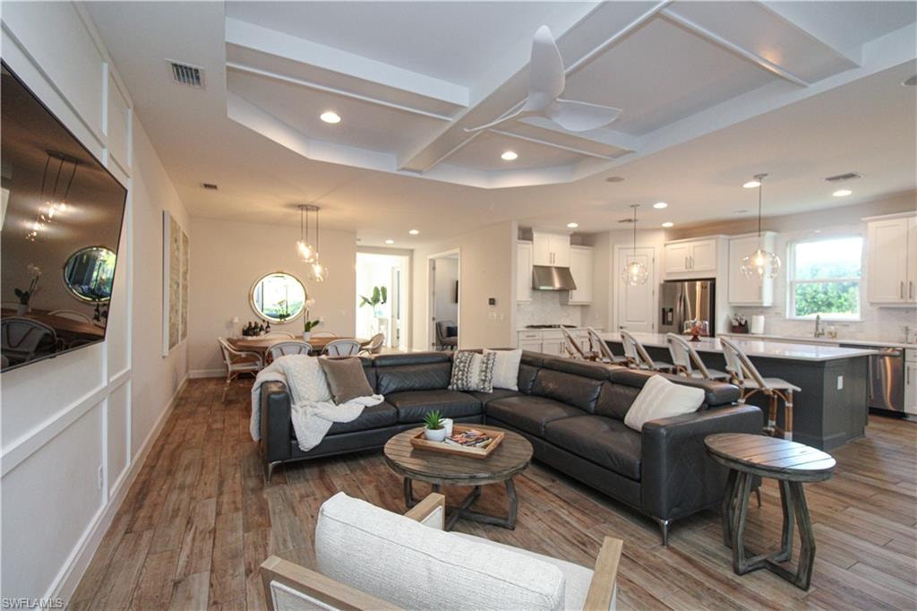 Living room with ceiling fan, light hardwood / wood-style floors, and coffered ceiling