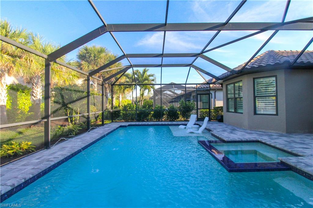 View of pool with glass enclosure, a patio area, and an in ground hot tub