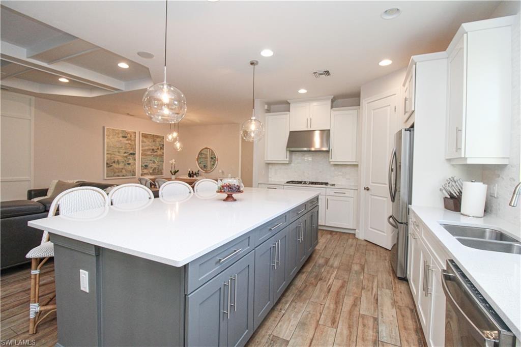 Kitchen featuring a breakfast bar, stainless steel appliances, white cabinetry, and light hardwood / wood-style floors