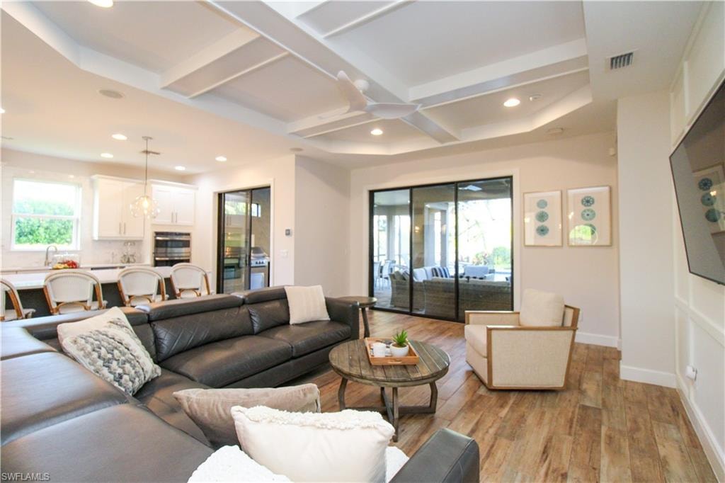 Living room featuring beamed ceiling, light hardwood / wood-style flooring, ceiling fan, and coffered ceiling