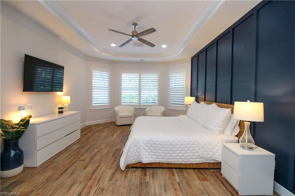 Bedroom with ceiling fan, light hardwood / wood-style floors, crown molding, and a tray ceiling