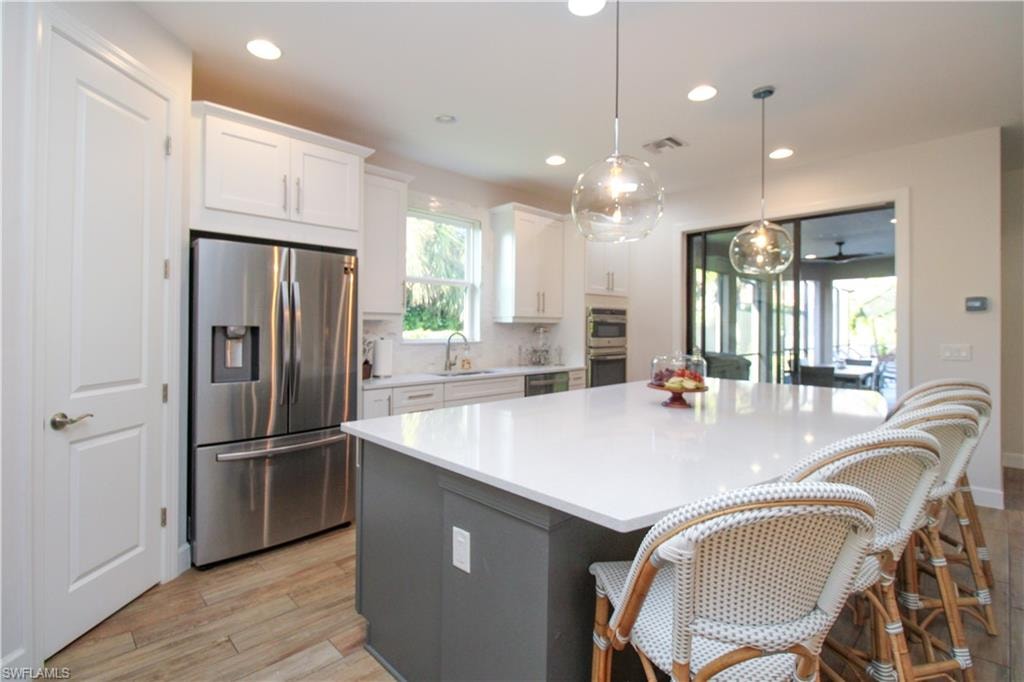 Kitchen featuring appliances with stainless steel finishes, light wood-type flooring, sink, pendant lighting, and white cabinetry