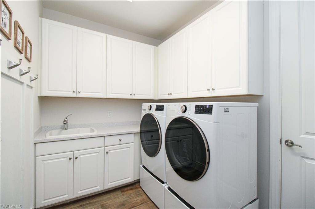 Laundry area with dark hardwood / wood-style floors, cabinets, sink, and washing machine and clothes dryer