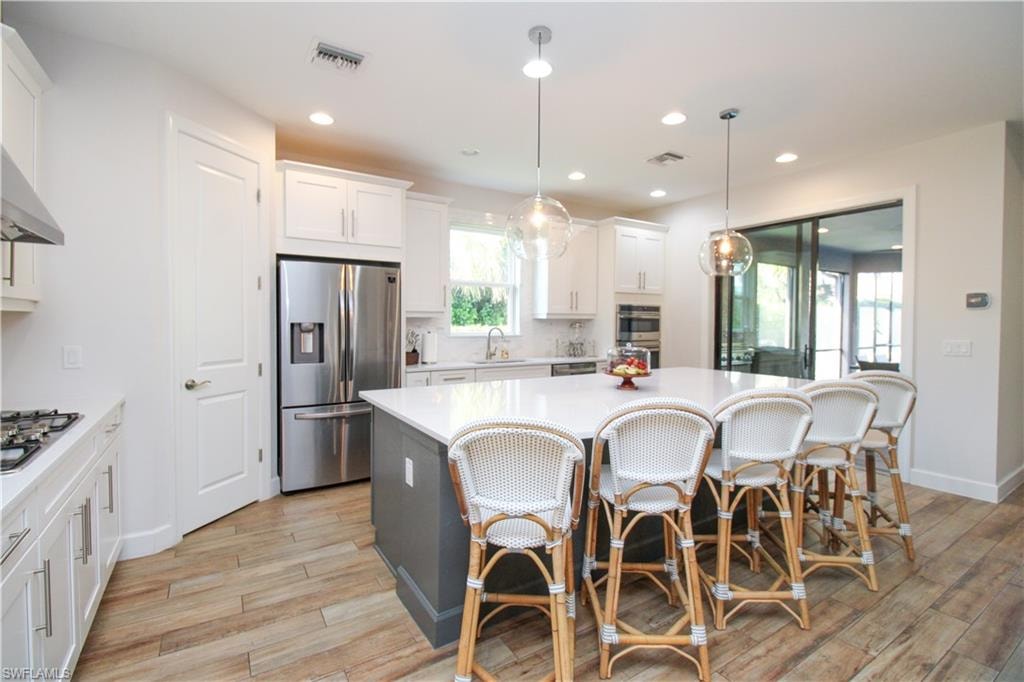 Kitchen with appliances with stainless steel finishes, light hardwood / wood-style flooring, a center island, white cabinetry, and hanging light fixtures