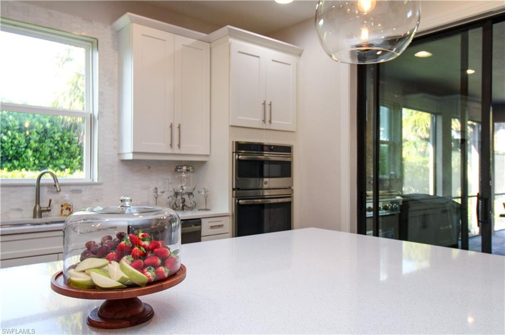 Kitchen with double oven, tasteful backsplash, white cabinets, and sink