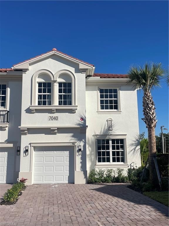 Mediterranean / spanish home with a tile roof, stucco siding, an attached garage, and decorative driveway