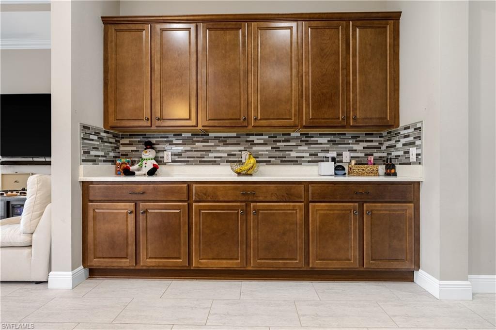 Kitchen with decorative backsplash, light tile patterned floors, and brown cabinets