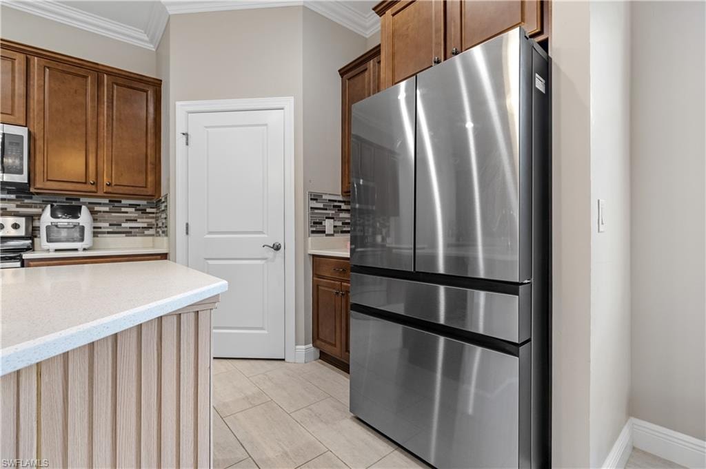 Kitchen featuring stainless steel appliances, ornamental molding, light stone counters, decorative backsplash, and light tile patterned floors