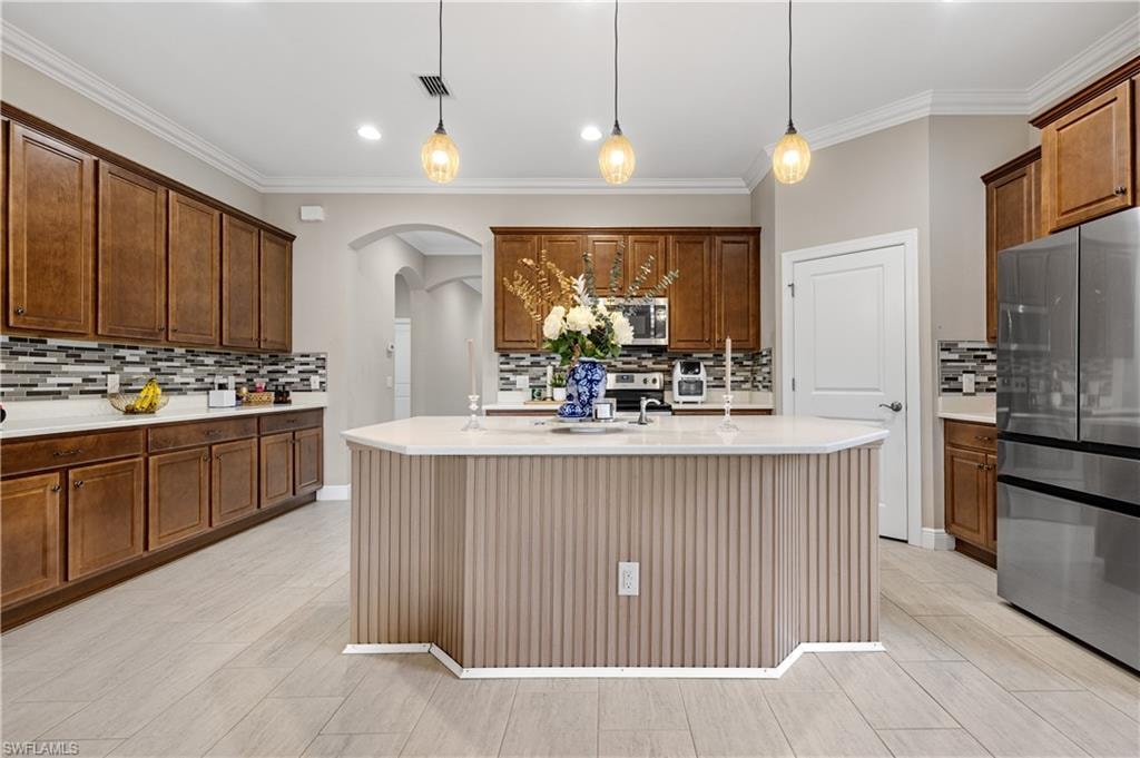 Kitchen with appliances with stainless steel finishes, arched walkways, pendant lighting, tasteful backsplash, and crown molding