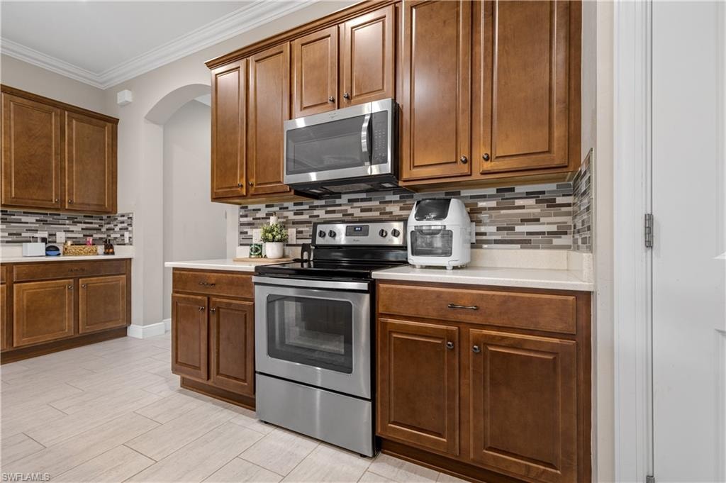 Kitchen featuring stainless steel appliances, backsplash, crown molding, brown cabinetry, and light wood-style floors
