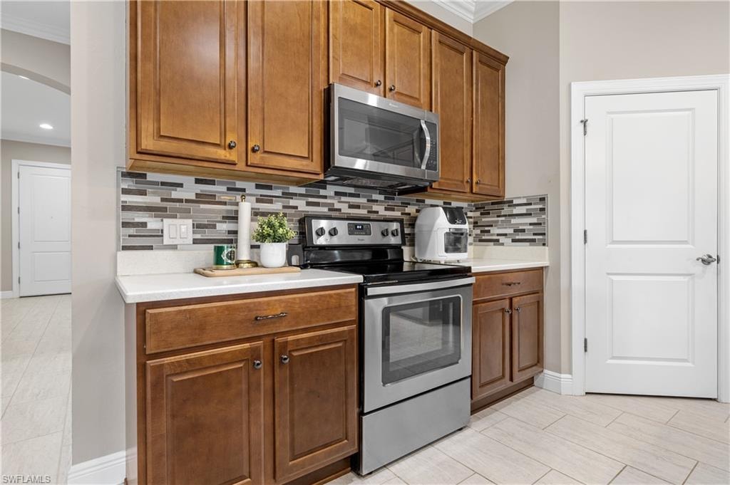 Kitchen with stainless steel appliances, crown molding, light countertops, backsplash, and brown cabinets