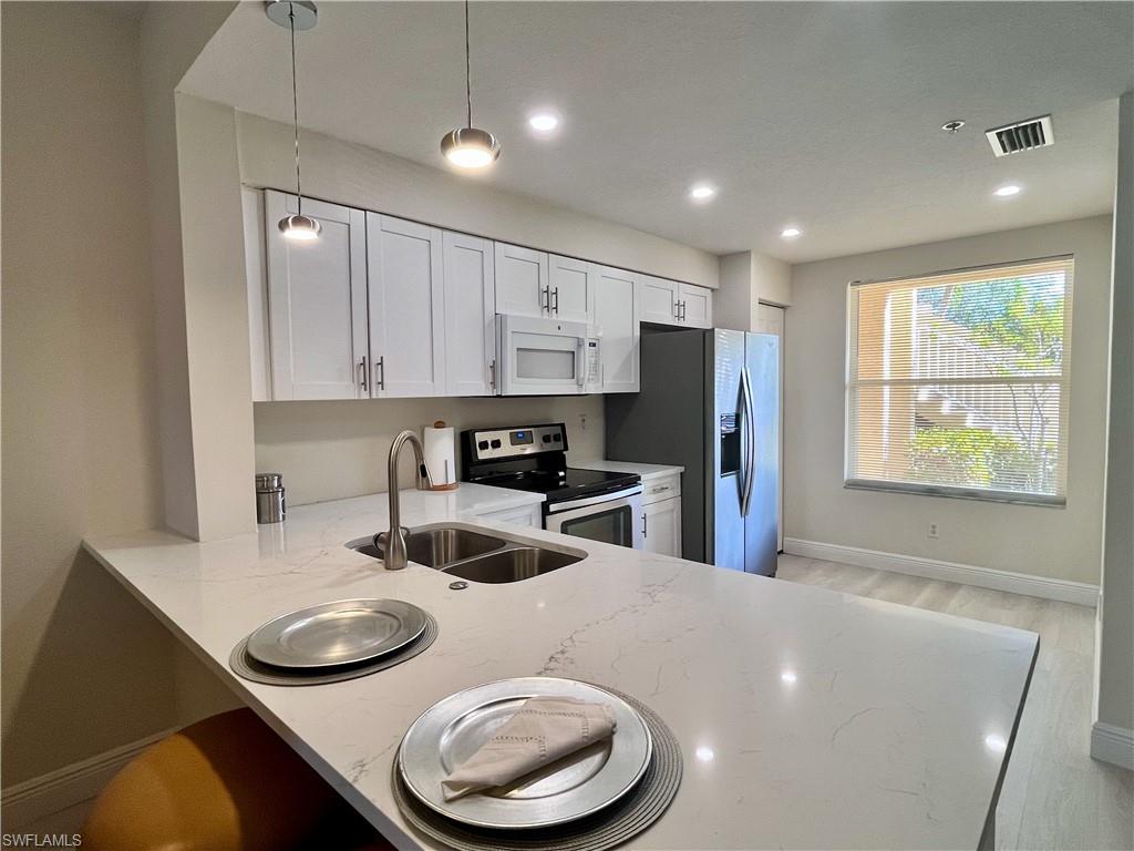 Kitchen featuring light stone countertops, stainless steel appliances, a peninsula, white cabinets, and hanging light fixtures
