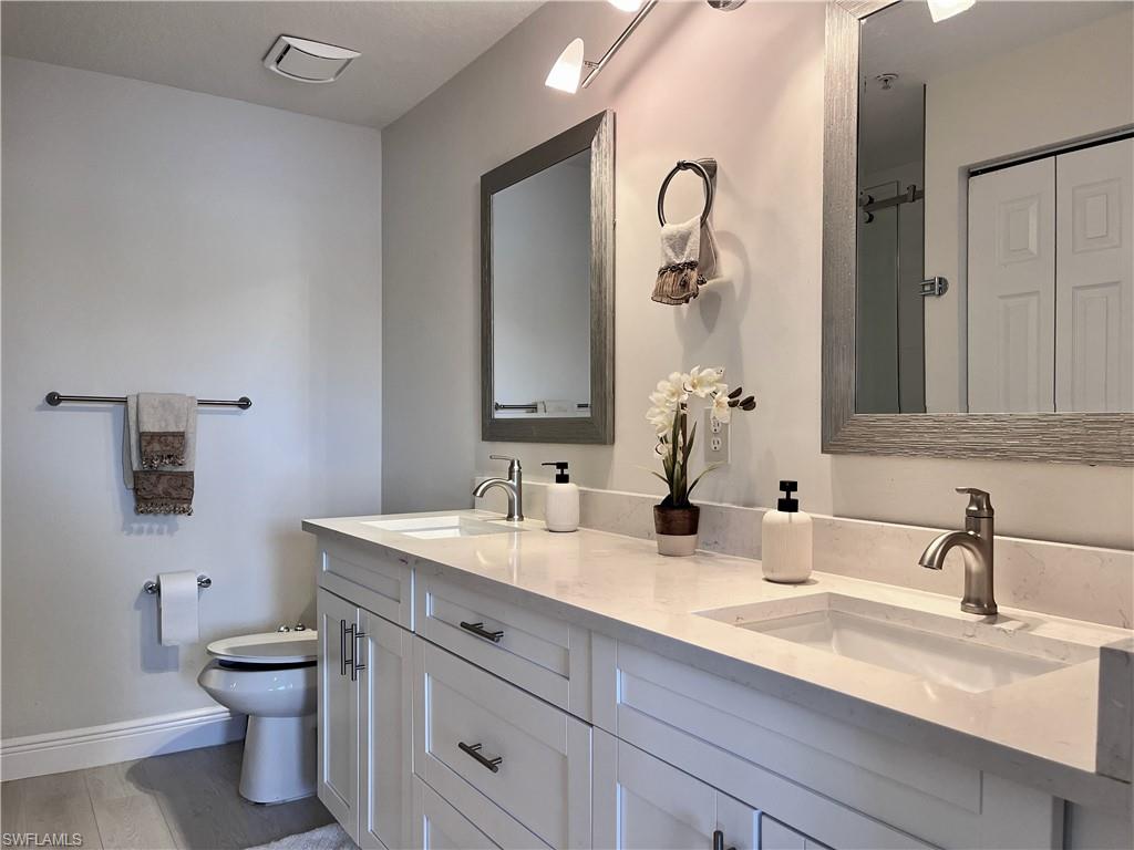 Full bathroom featuring double vanity, a shower with shower door, and light wood-style floors