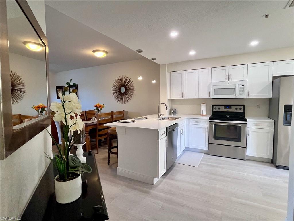 Kitchen featuring stainless steel appliances, a peninsula, white cabinetry, a kitchen breakfast bar, and light wood-style floors