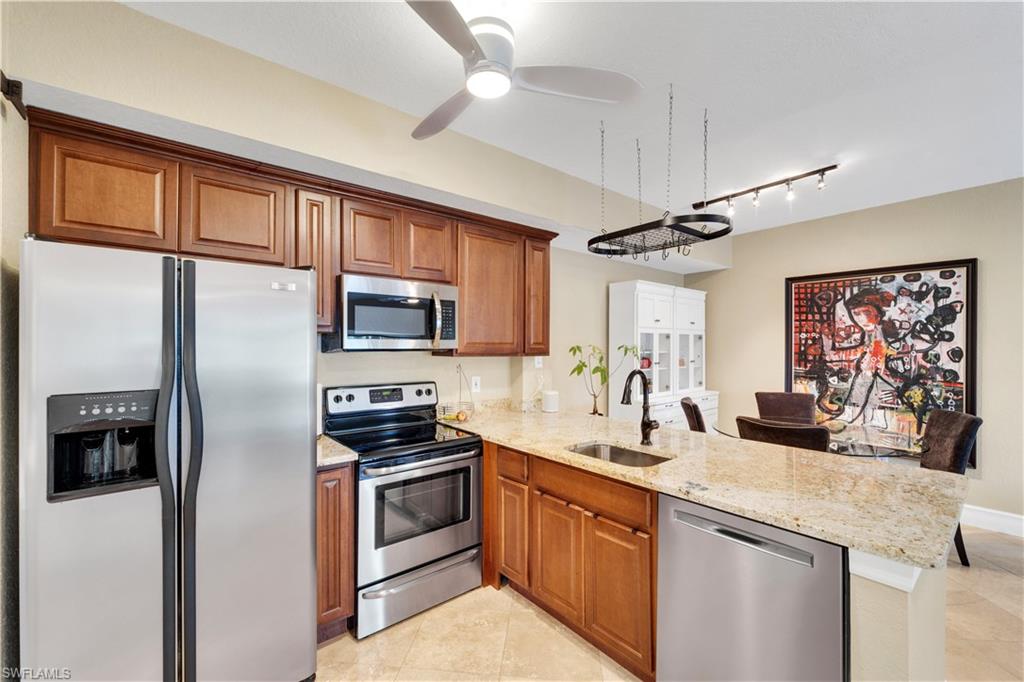 Kitchen featuring stainless steel appliances, brown cabinetry, light stone counters, a peninsula, and light tile patterned floors