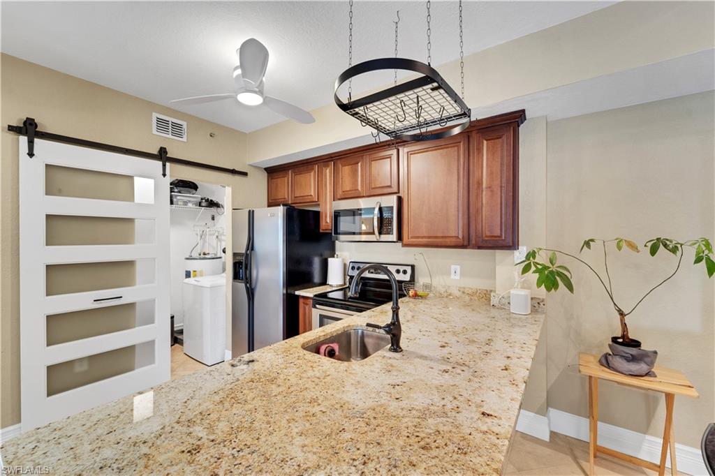 Kitchen featuring light stone counters, appliances with stainless steel finishes, a barn door, washer / dryer, and light tile patterned flooring