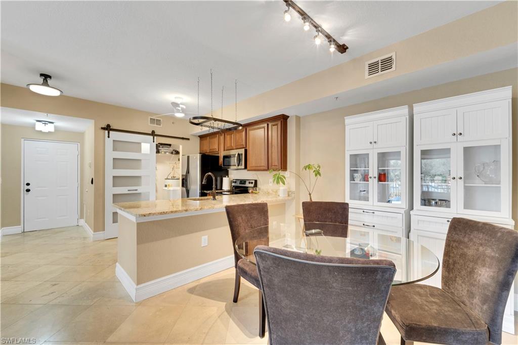 Kitchen featuring a barn door, light stone countertops, a peninsula, brown cabinets, and stainless steel appliances