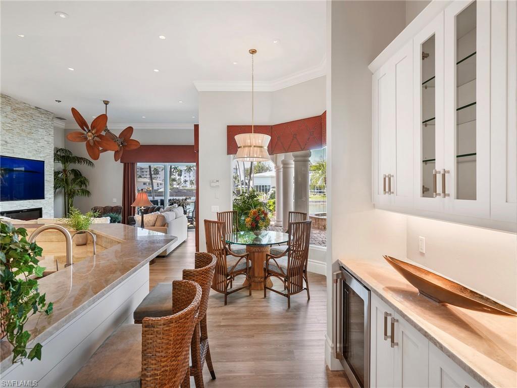 Dining space with beverage cooler, crown molding, dark wood-type flooring, a stone fireplace, and recessed lighting