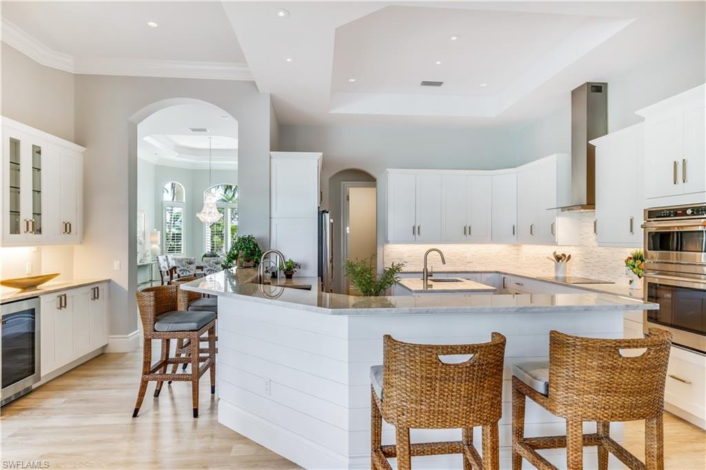 Kitchen with a kitchen bar, arched walkways, white cabinetry, and ornamental molding