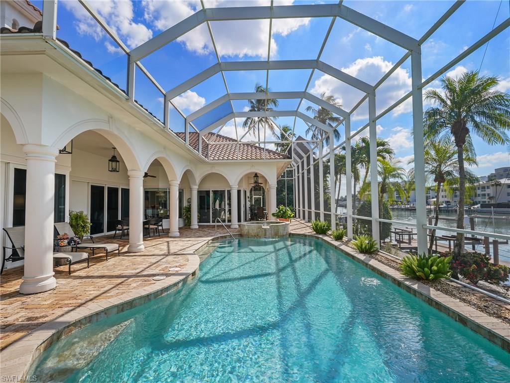 View of pool featuring a sunroom, a patio area, glass enclosure, a pool with connected hot tub, and a water view