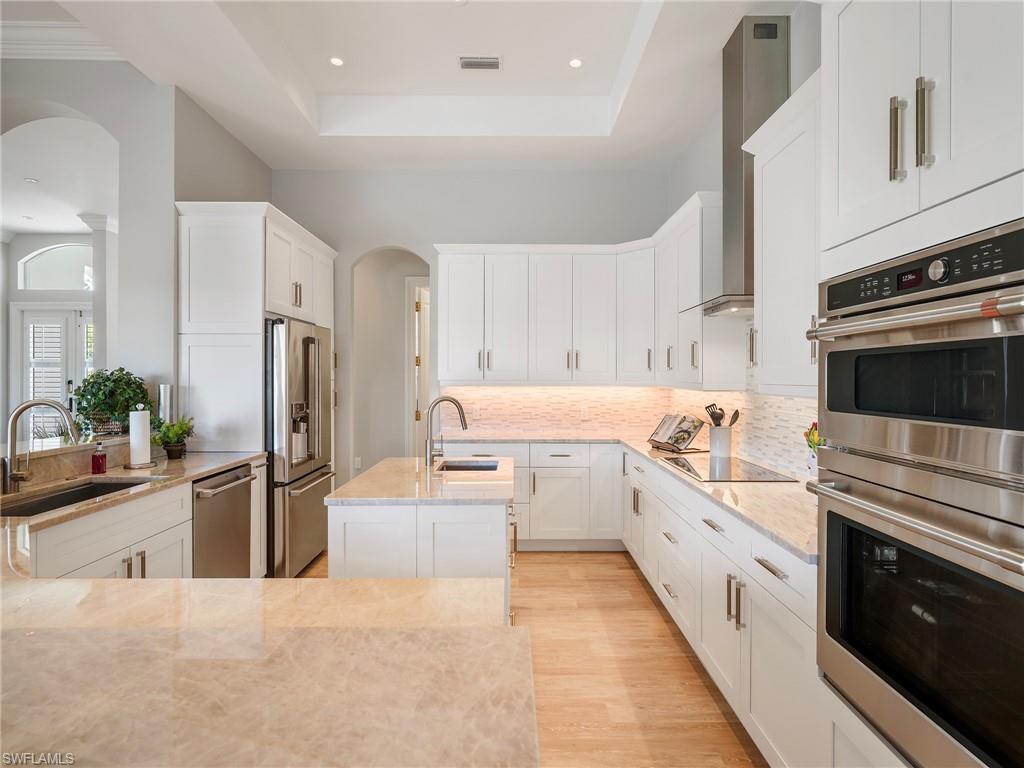 Kitchen with stainless steel appliances, arched walkways, light stone counters, white cabinets, and a tray ceiling