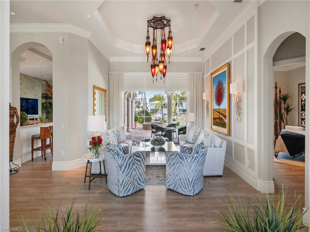 Living area with arched walkways, wood finished floors, ornamental molding, a tray ceiling, and a chandelier