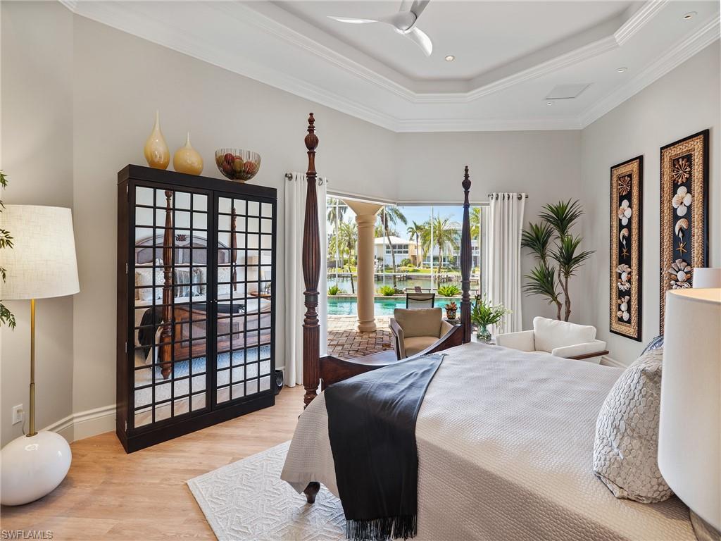 Bedroom featuring light wood finished floors, ornamental molding, access to outside, and a raised ceiling