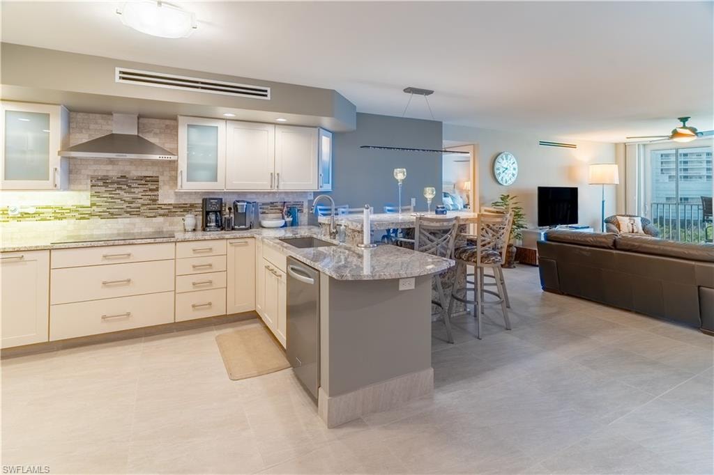Kitchen featuring a peninsula, open floor plan, light stone countertops, backsplash, and wall chimney range hood