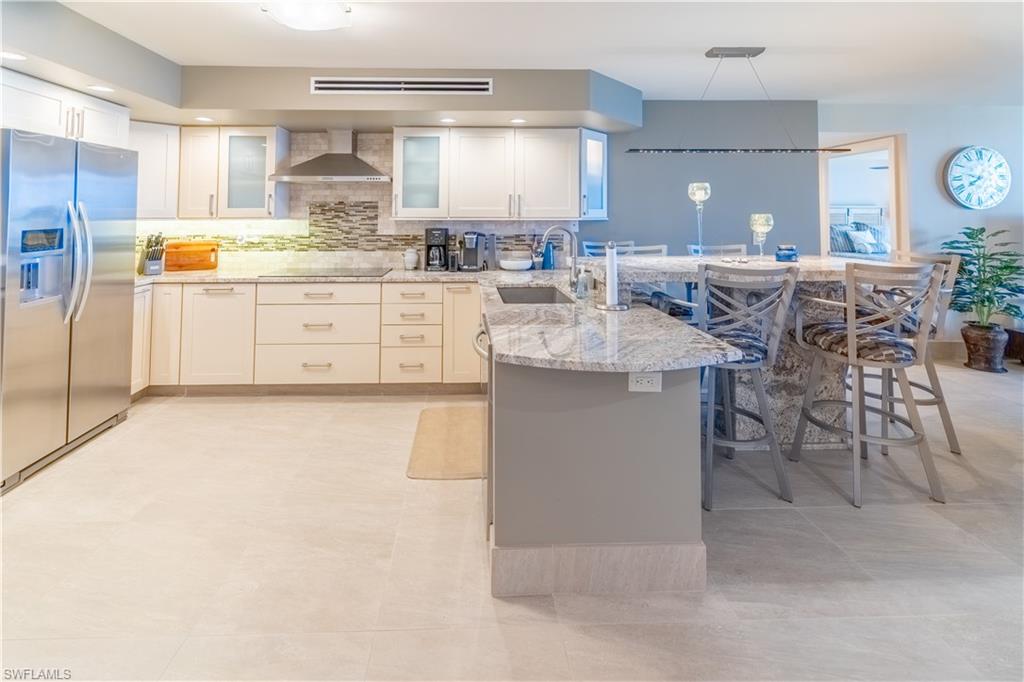 Kitchen featuring a breakfast bar, stainless steel refrigerator with ice dispenser, a peninsula, white cabinetry, and decorative backsplash