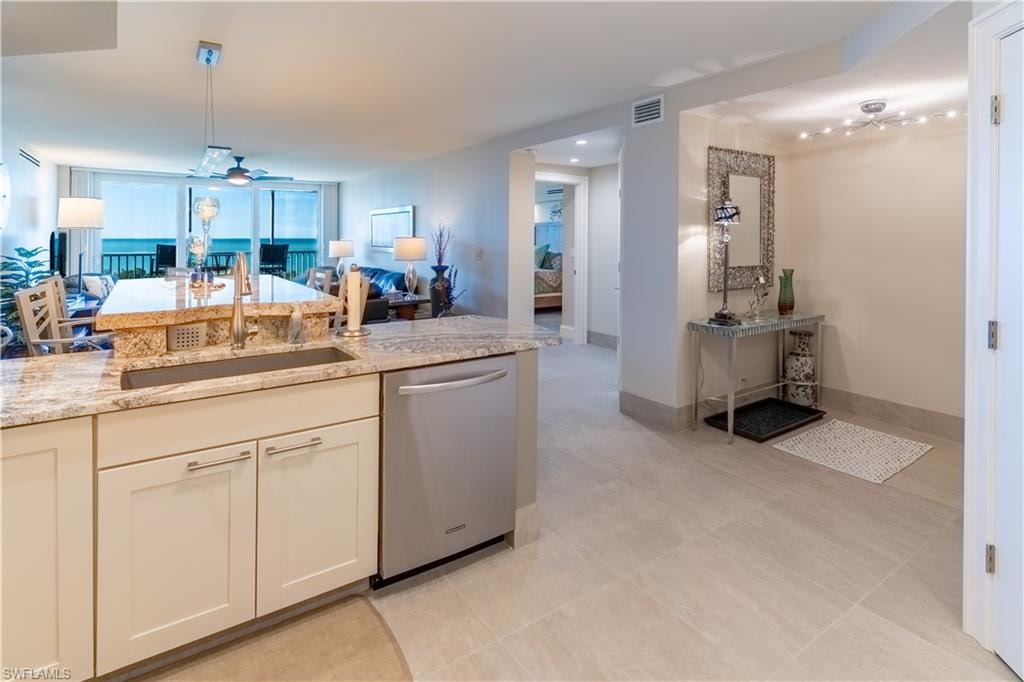 Kitchen featuring open floor plan, a ceiling fan, dishwasher, light stone countertops, and decorative light fixtures