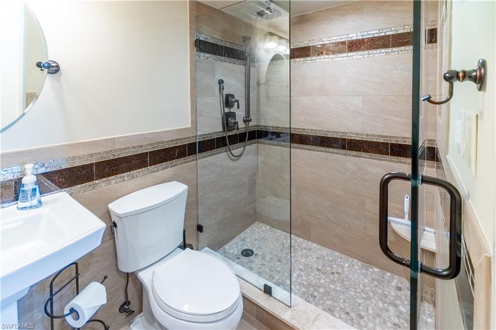Bathroom featuring a shower stall, tile walls, and a wainscoted wall