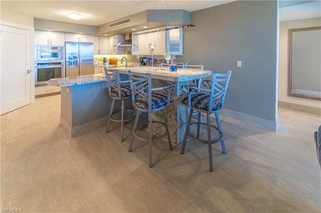 Kitchen featuring a peninsula, a kitchen bar, light stone counters, stainless steel refrigerator with ice dispenser, and white cabinetry